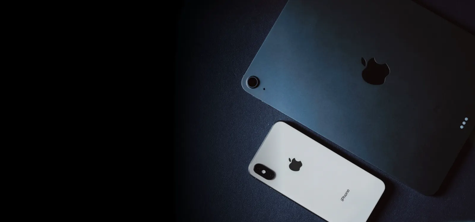 An iPad and iPhone resting on a dark surface